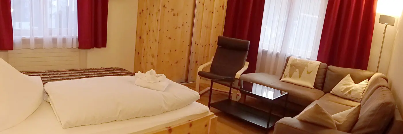 Wohn-Schlafzimmer mit Couchgarnitur und Betten, rote Vorhänge