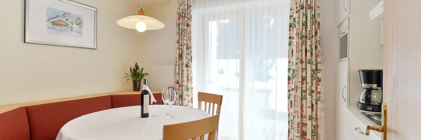 Gedeckter Tisch mit Eckbank in der Wohnung F, dahinter die Terrassentür